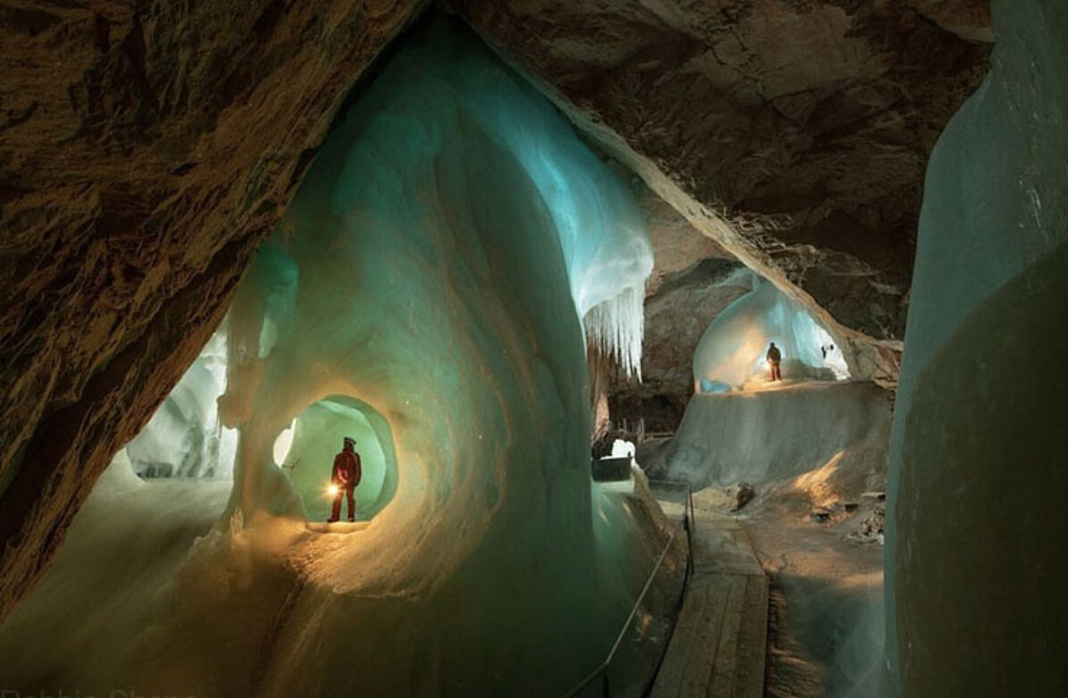 A person in a red jacket stands in a large ice formation in the ice giant world, while another person, surrounded by ice walls, goes on a voyage of discovery further ahead.