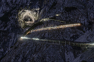A winding mountain path, illuminated by strips of light at night, leads up to the large cave entrance of the Ice Giant World, which is impressively situated between dramatic rocky cliffs.