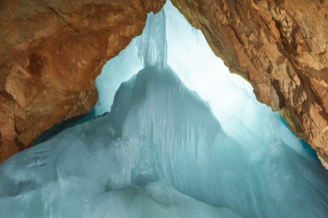Eine große Eisformation mit Eiszapfen umgeben von rotbraunen Felswänden.