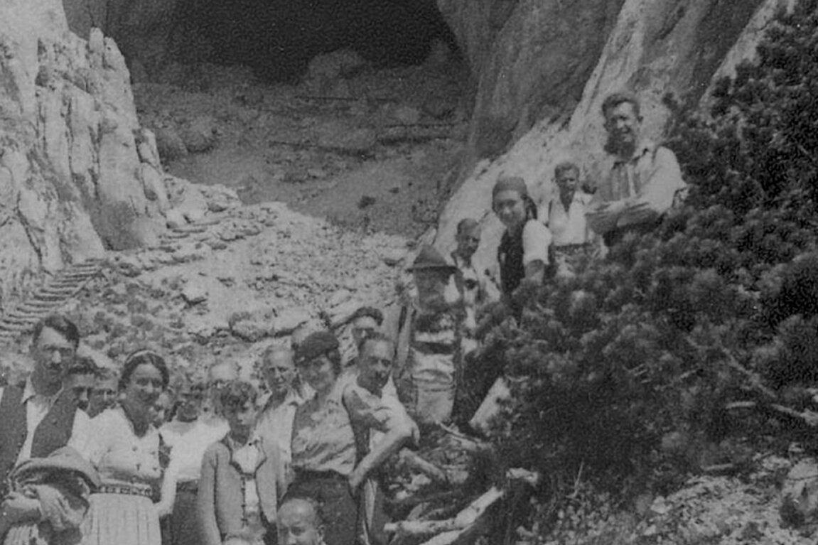 Eine Gruppe von Menschen posiert im Freien auf felsigem Gelände vor dem Eingang der Eisriesenwelt