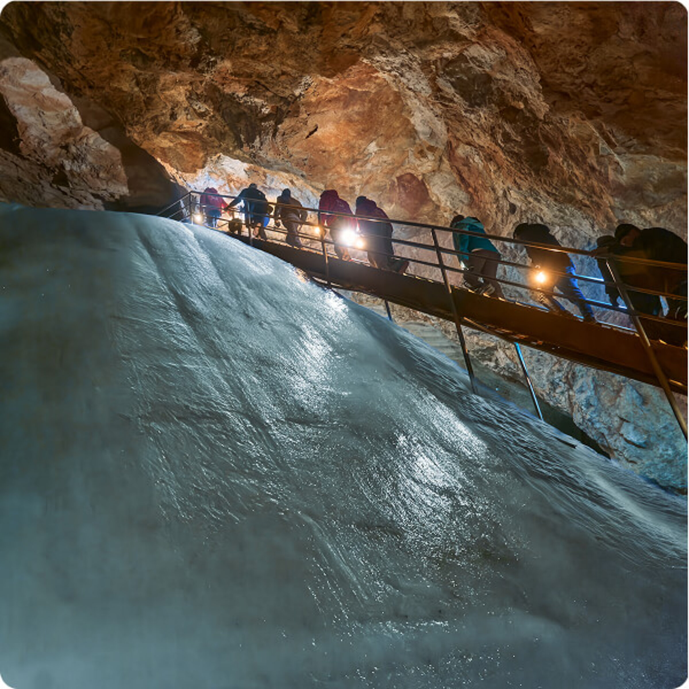 Ein Höhlenführer in einer roten Jacke steht mit einer Laterne in der Hand in der Eishöhle der Eisriesenwelt, umgeben von Eisformationen.