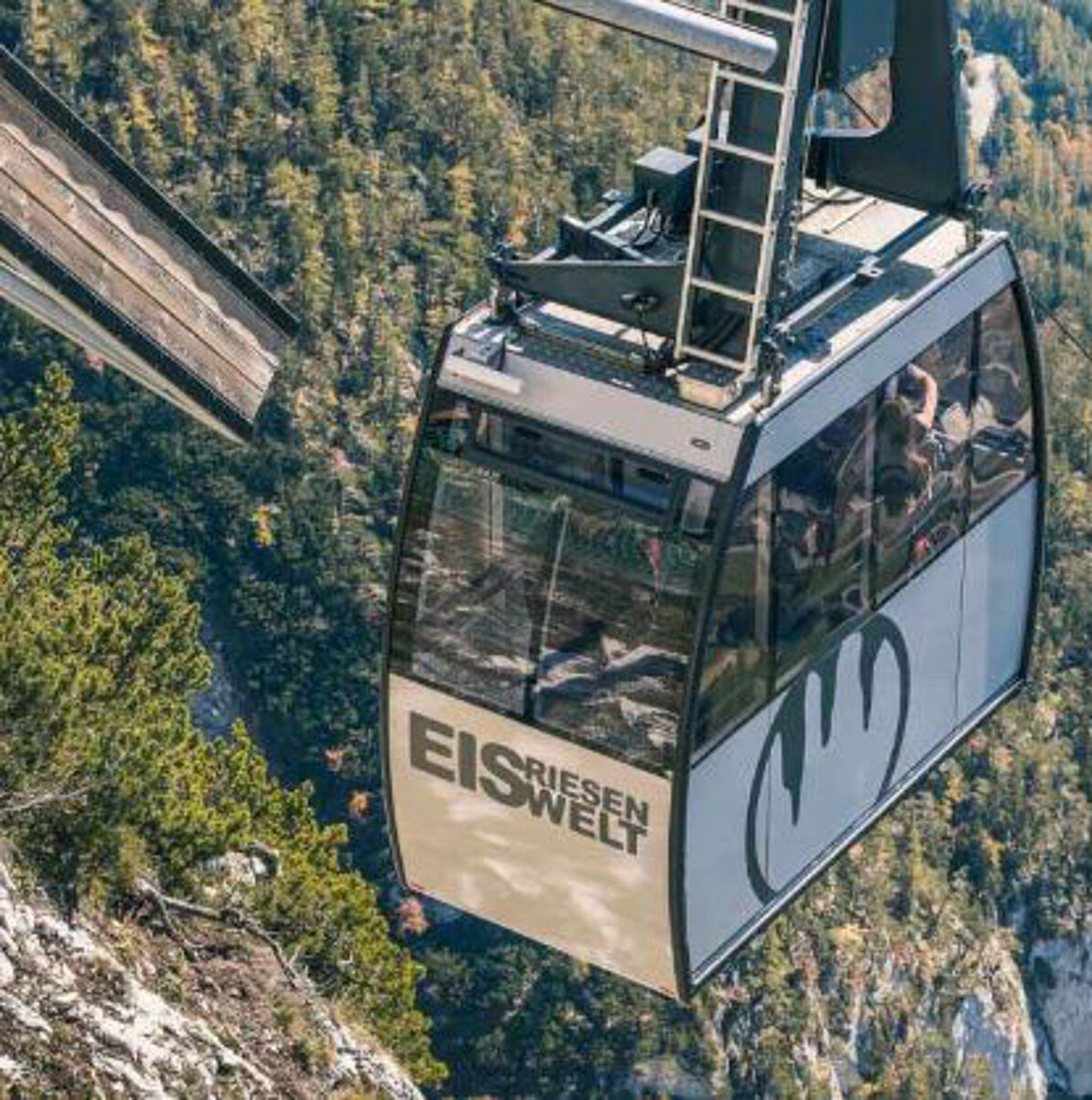 Eine Seilbahn mit der Aufschrift „Eisriesenwelt Seilbahn“ fährt über einen steilen, bewaldeten Berghang und befördert die Passagiere hoch über dem Boden zur Seilbahnbergstation.