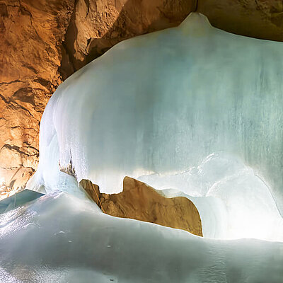 [Translate to Englisch:] Eine Eisformation in der Eisriesenwelt mit felsigen, braunen Wänden; Licht fällt auf das Eis
