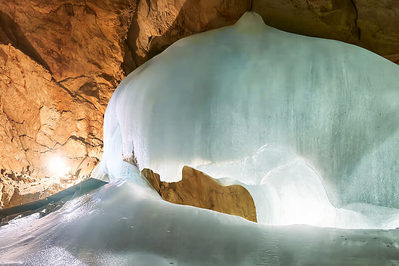 [Translate to Englisch:] Eine Eisformation in der Eisriesenwelt mit felsigen, braunen Wänden; Licht fällt auf das Eis